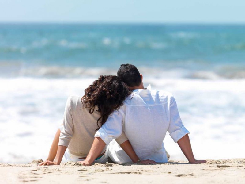 Rear view of a couple sitting on beach with woman leaning head on man's shoulder